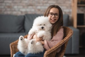 ילדה שמחה מחזיקה כלב יושבת על כורסא בחדר